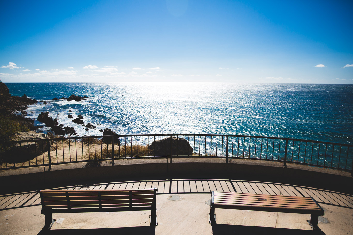 Scenic view of two benches overlooking the ocean and a blue sky.